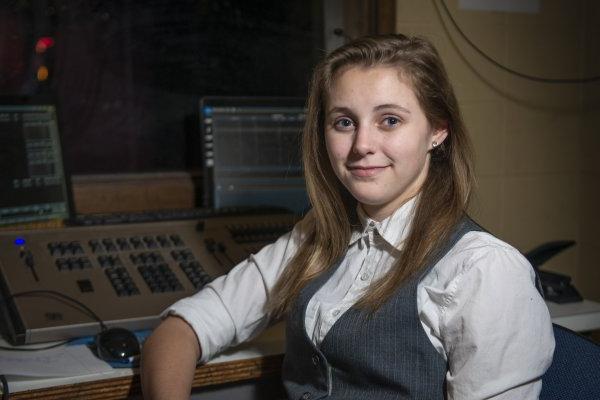 Crystal Hayner, with long brown hair, wearing a vest, sits by a computer set-up.